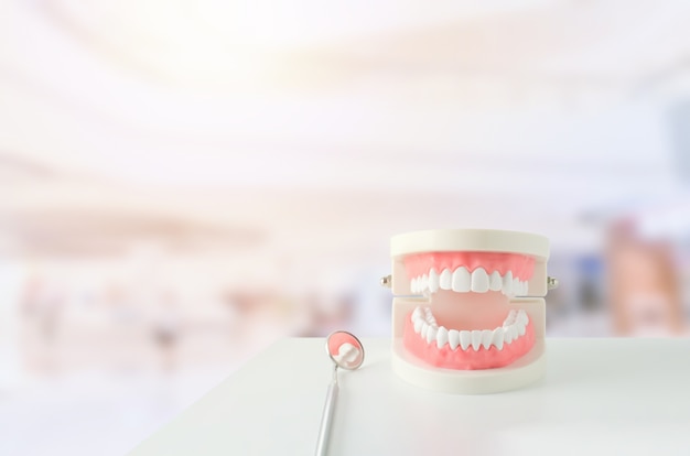 Photo gros plan du modèle de dents blanches avec gomme rouge et miroir dentaire sur arrière-plan flou