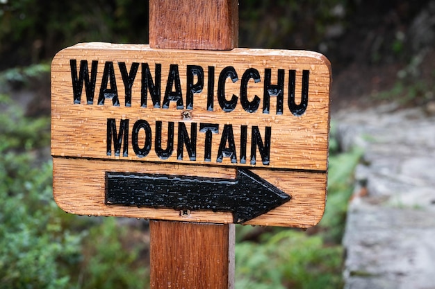 Gros plan du panneau de pointage en bois avec étiquette noire à la montagne waynapicchu couverte de gouttes