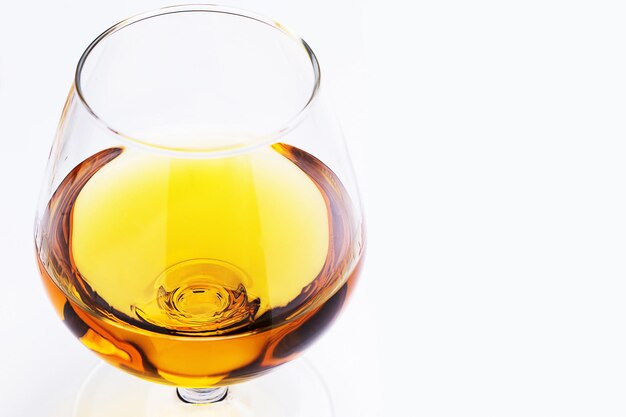 Gros plan du petit verre rempli d'un cognac sur fond blanc