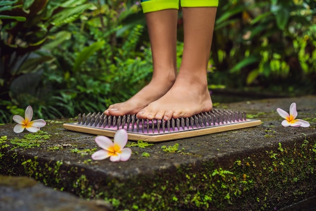 Photo gros plan du pied de la fille dans les leggings pour le yoga qui se dresse sur la planche avec des clous