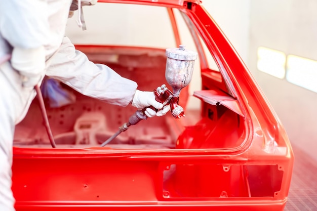 Photo gros plan du pistolet à peinture en aérosol avec travailleur travaillant sur une voiture rouge