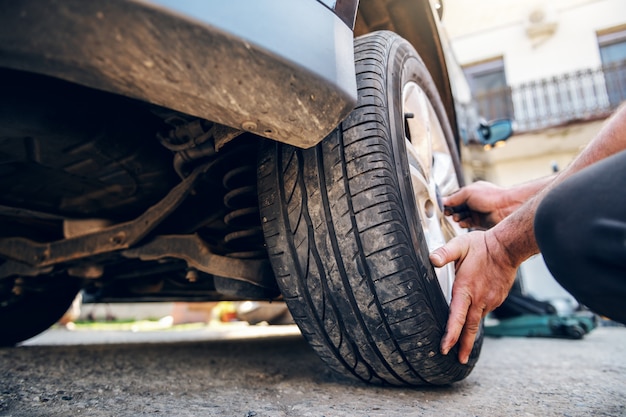 Gros plan du pneu de changement de mécanicien automobile en s'accroupissant à l'atelier.