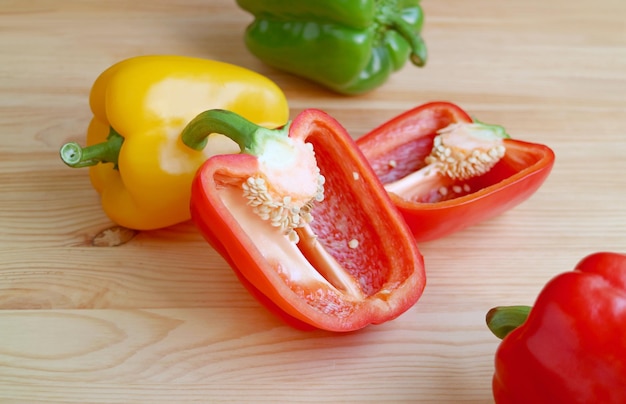 Gros plan du poivron rouge coupé avec des poivrons tricolores éparpillés sur une table en bois