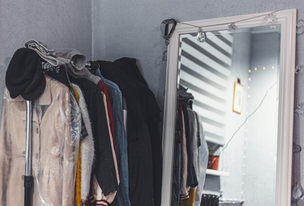 Gros plan du rack avec des vêtements sur des cintres près de grand miroir blanc.