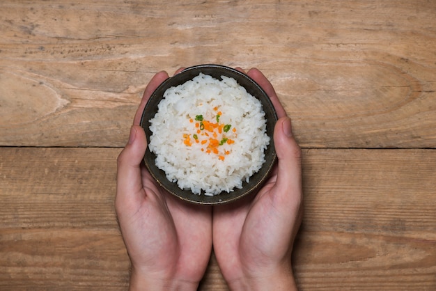 Photo gros plan du riz cuit dans un bol en bois tenant à la main sur une table en bois
