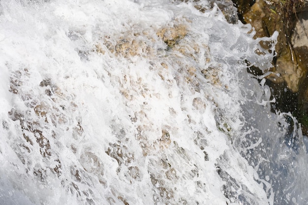 Gros plan du ruisseau cascade de la rivière coule sur des pierres moussues bouillonnant d'eau de cascade avec du blanc