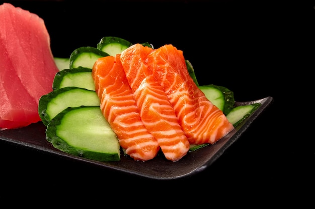 Gros plan du sashimi de saumon cru sur un plateau avec du thon et du concombre sur fond noir