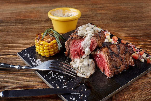 Gros plan du steak de boeuf grillé frais avec sauce aux champignons à la crème sur tableau noir sur fond de bois