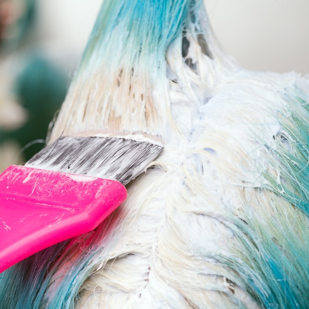 Gros plan du styliste à l'aide d'un pinceau rose tout en appliquant de la peinture à une cliente avec une couleur de cheveux émeraude