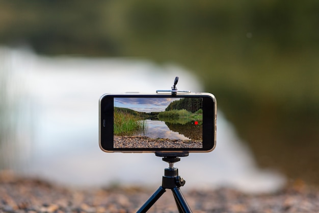 Un gros plan du téléphone sur un trépied prend une vidéo ou une photo de la nature. Un beau lac dans la forêt avec des nuages sur l'écran du téléphone portable du photographe.