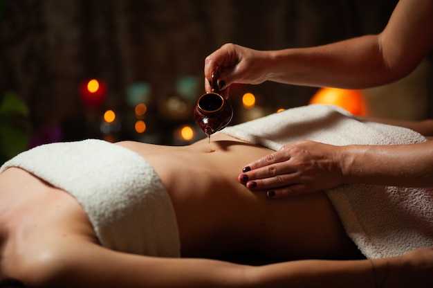 Gros plan du thérapeute faisant un massage du ventre sur la femme dans le spa contre l'obscurité.