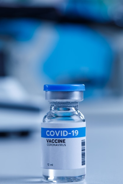 Gros plan du vaccin contre le coronavirus covid 19 dans un petit flacon en verre utilisé pour la protection contre les injections sur le bureau du laboratoire devant un microscope scientifique arrière-plan flou à l'hôpital.