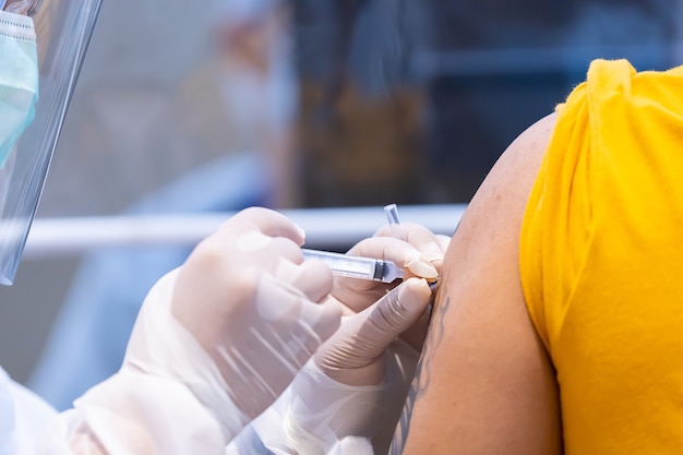 Photo gros plan du vaccin covid-19 injecté dans l'épaule du bras du patient avec une seringue en plastique à usage unique par le médecin, renforce le système immunitaire avec un virus inactivé ou adénovirus