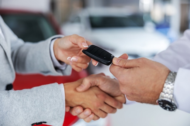 Gros plan du vendeur de voitures et d'un acheteur se serrant la main en se tenant debout dans un salon de voiture. Vendeur remettant les clés de voiture à un acheteur.