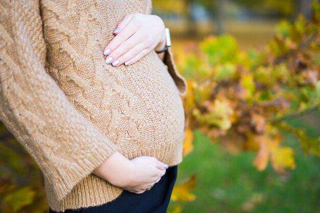 Gros plan du ventre de femme enceinte sur fond de parc automne