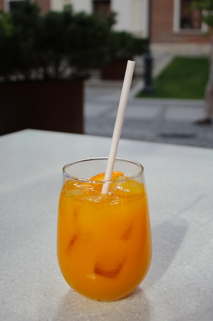 Gros plan du verre avec un cocktail d'été et une paille en papier écologique sur une table de terrasse de café blanc