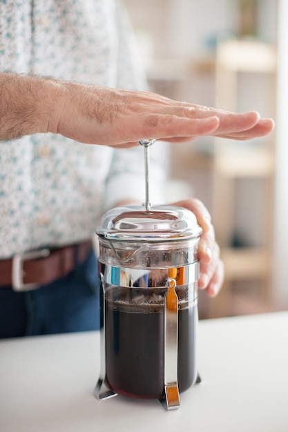 Gros plan du vieil homme faisant du café avec une presse française. Une personne âgée le matin profitant d'une tasse d'expresso de café brun frais de la caféine d'une tasse vintage, d'un rafraîchissement de détente de filtre