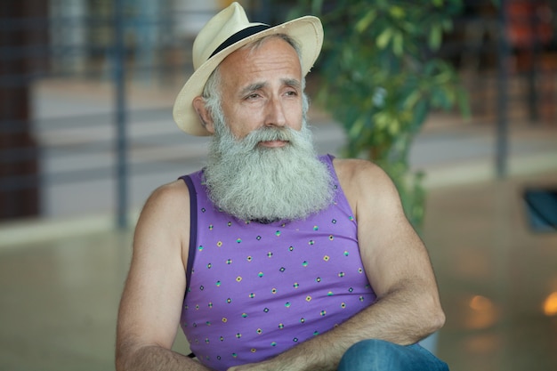 Photo gros plan du vieil homme hipster avec barbe et moustache portant une chemise violette et un chapeau fedora en paille.