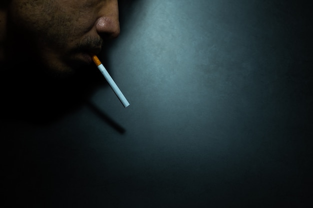 Gros plan du visage des hommes fument une cigarette dans l&#39;obscurité