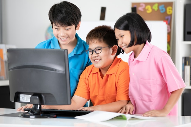 Gros plan d&#39;élèves asiatiques souriants à l&#39;aide d&#39;un ordinateur de bureau.