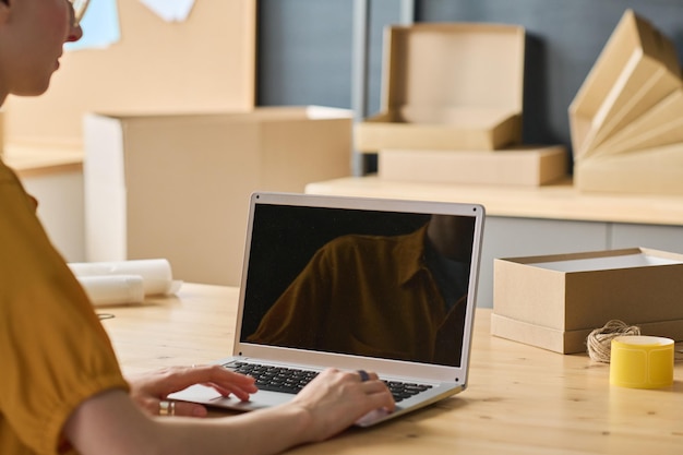 Gros plan d'employé d'entrepôt assis à table et travaillant en ligne sur un ordinateur portable