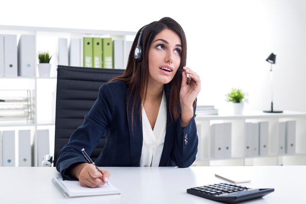 Gros plan d'une employée du service d'assistance à la clientèle sur son lieu de travail dans un bureau blanc. Elle parle dans le casque