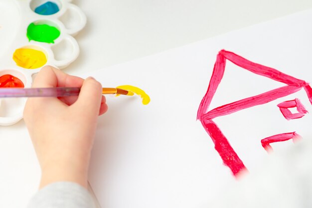 Gros plan sur l'enfant qui commence à dessiner le soleil sur la maison sur du papier blanc.