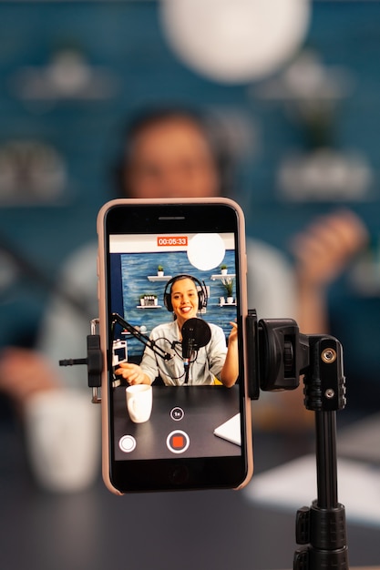 Gros plan sur l'enregistrement en direct d'un vlogger d'influence en regardant un smartphone sur un trépied dans un podcast home studio. Créateur de contenu créatif créant une vidéo en ligne pour le public des abonnés