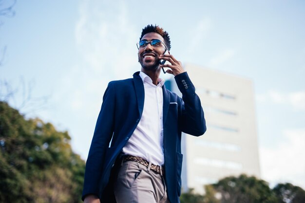 Gros plan sur un entrepreneur noir marchant dans la rue tout en utilisant son téléphone pour faire des affaires