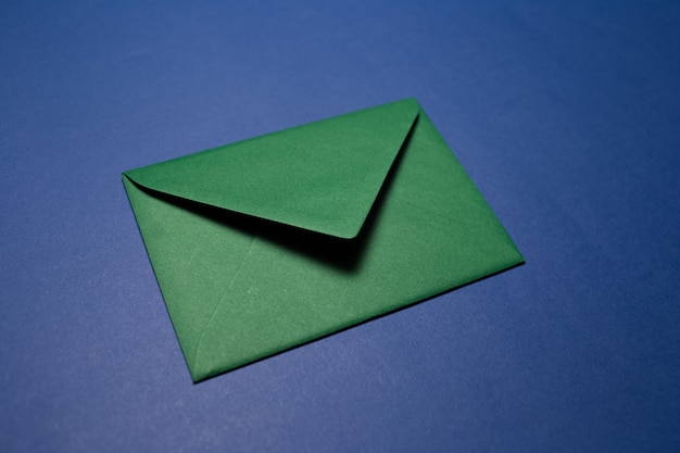 Gros plan d'enveloppe de papier de couleur verte isolée sur un mur bleu texturé.