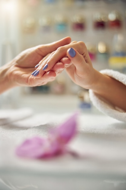 Gros plan d'une esthéticienne tenant des doigts de femme avec une manucure de couleur sur une table avec une orchidée