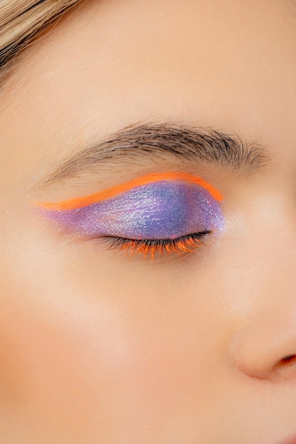 Gros plan sur un eye-liner violet et orange avec des paillettes