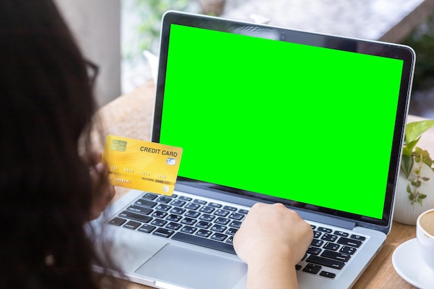 Gros plan d'une femme d'affaires indépendante tenant à la main des cartes de crédit travaillant à l'aide d'un ordinateur portable avec une tasse de café dans un café comme l'arrière-plan Concept de paiement en ligne