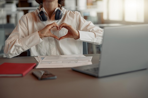 Gros plan sur une femme d'affaires travaillant sur un ordinateur portable assis dans un café confortable et montrant un signe d'amour