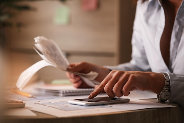 Photo gros plan sur une femme d'affaires utilisant un téléphone intelligent tout en calculant ses factures au bureau