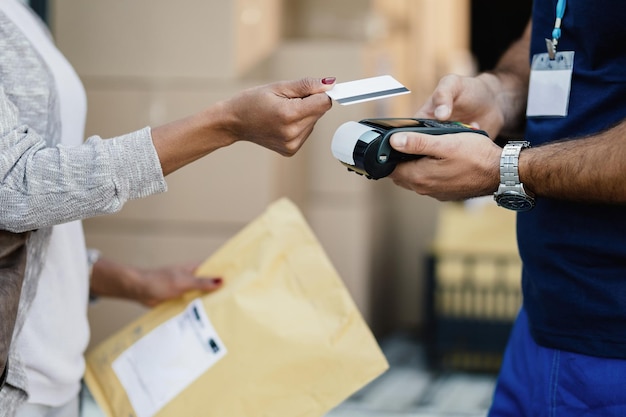 Gros plan d'une femme afro-américaine effectuant un paiement sans contact à un coursier pour la livraison d'un colis