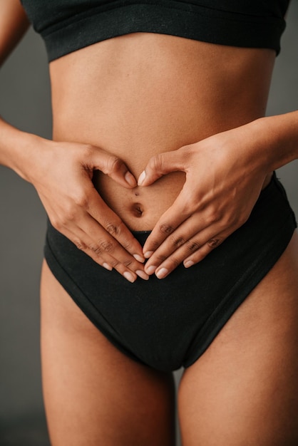 gros plan sur une femme afro-américaine en forme de coeur avec ses mains sur son ventre