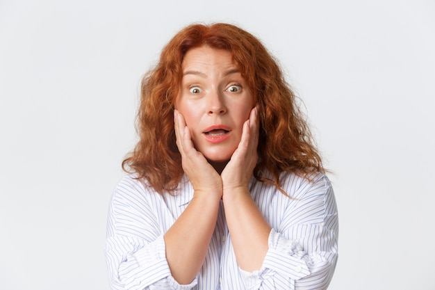 Gros plan d'une femme d'âge moyen surprise et heureuse, jolie rousse touchant les joues