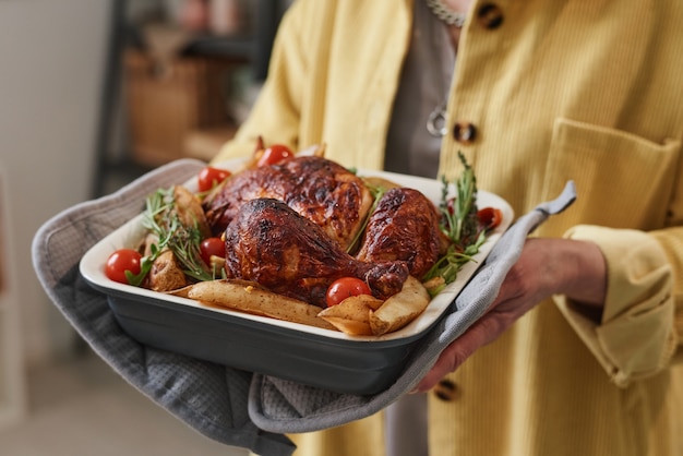 Gros plan d'une femme âgée tenant un plat avec du poulet rôti et des légumes