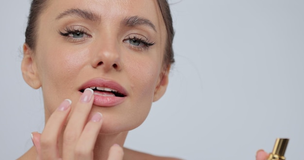 Gros plan, femme, appliquer, rouge lèvres, sourire, appareil-photo, confection, maquillage, poser, gris, studio, fond, concept cosmétique