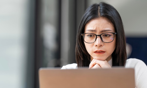 Gros plan d'une femme asiatique fatiguée et stressée avec des lunettes assise au bureau