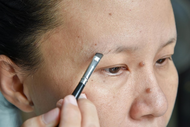 Gros plan d'une femme asiatique se maquiller avec une brosse à sourcils