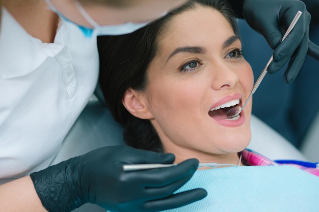 Gros plan d'une femme assise avec la bouche ouverte et un dentiste attentif regardant ses dents avec un miroir buccal