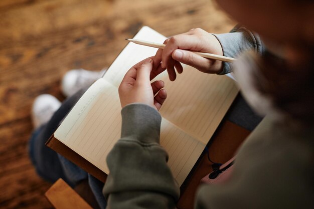 Gros plan d'une femme assise avec un cahier sur ses genoux et y écrivant ses plans ou faisant ses devoirs