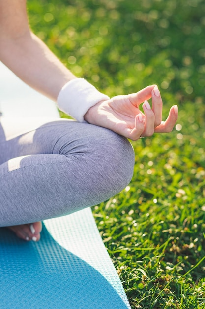 Gros plan d'une femme assise en position du lotus sur le tapis de yoga dans le parc