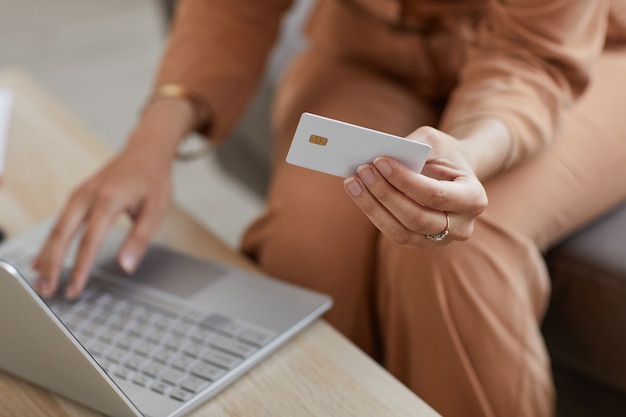 Gros plan d'une femme assise à la table à l'aide d'un ordinateur portable et de payer en ligne par carte de crédit pour les achats