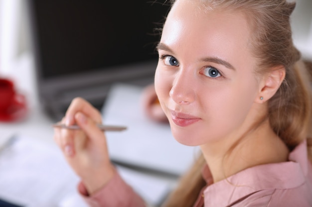 Gros plan de femme assistante souriante regardant la caméra avec joie. Documents de signature de bonne humeur. Blonde posant au bureau. Concept d'entreprise et d'entreprise