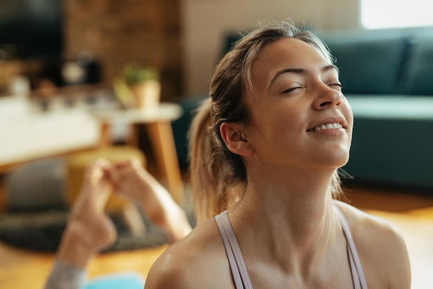 Gros plan d'une femme athlétique souriante faisant des exercices de relaxation après un entraînement sportif à la maison