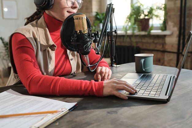 Photo gros plan sur une femme au casque assise à la table et travaillant sur un ordinateur portable dans un studio de radio