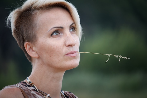 Gros plan d'une femme blonde d'âge moyen avec un épillet dans la bouche.